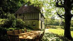 Uma casa tradicional em estilo Tudor, com fachada de pedra, deck de madeira e área de refeições com mesa e cadeiras.