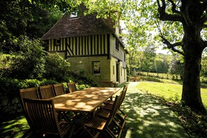 Een huis in traditionele Tudor-stijl met een stenen gevel, een houten terras en een eethoek met een tafel en stoelen.