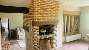 Quarto com lareira de tijolos, radiador branco, mobiliário de vime e vista para uma janela com persianas de madeira.
