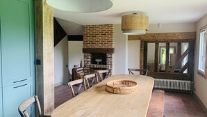 Uma sala de jantar com lareira de tijolos, mesa de madeira, cadeiras e luminária pendente.