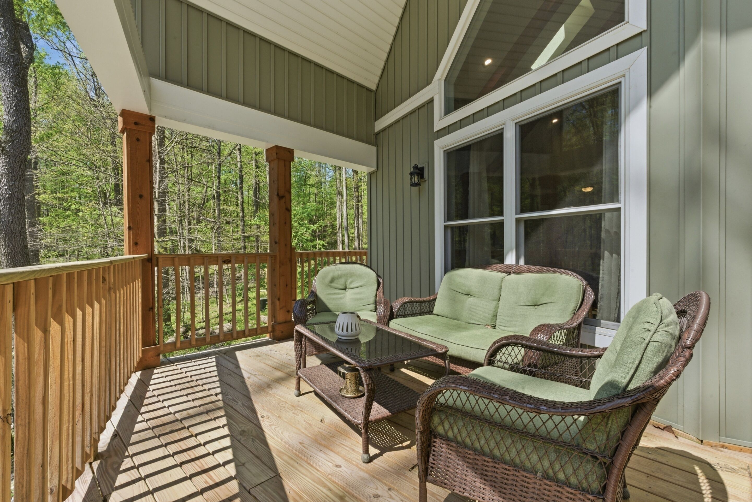A covered porch with wicker furniture, a glass table, and a view of a forest.