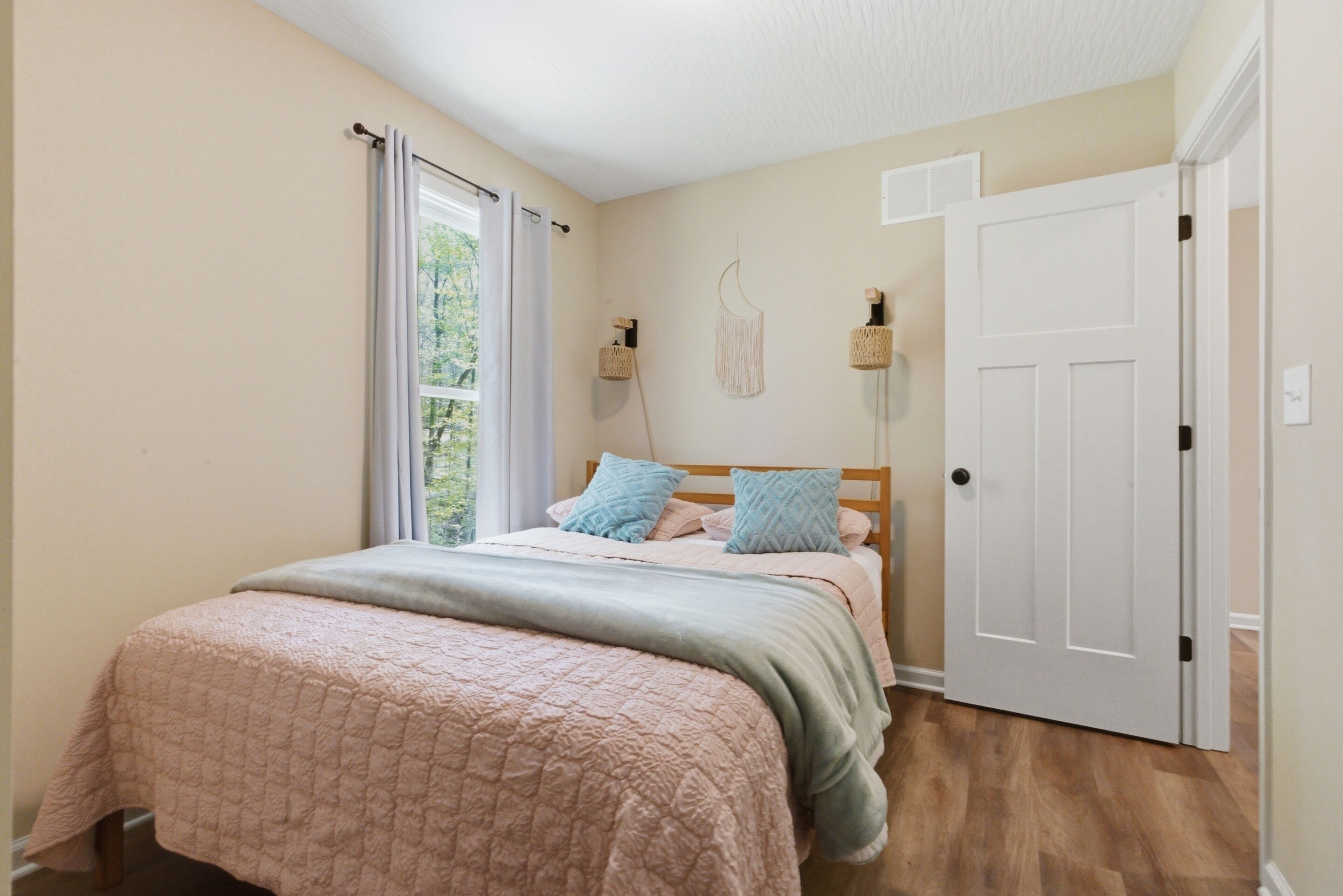 Une chambre à coucher avec un lit, une fenêtre avec des rideaux, une porte et des lampes fixées au mur.