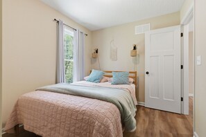 A bedroom with a bed, a window with curtains, a door, and wall-mounted lamps.