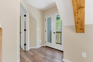 Un couloir doté d’un plancher en bois, d’une porte blanche avec un panneau de verre et d’une poutre en bois fixée au mur.