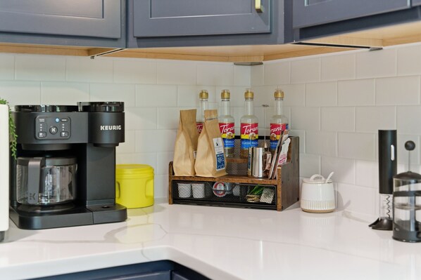 A kitchen with a Keurig coffee maker, Torani syrups, a yellow container, and a coffee grinder.