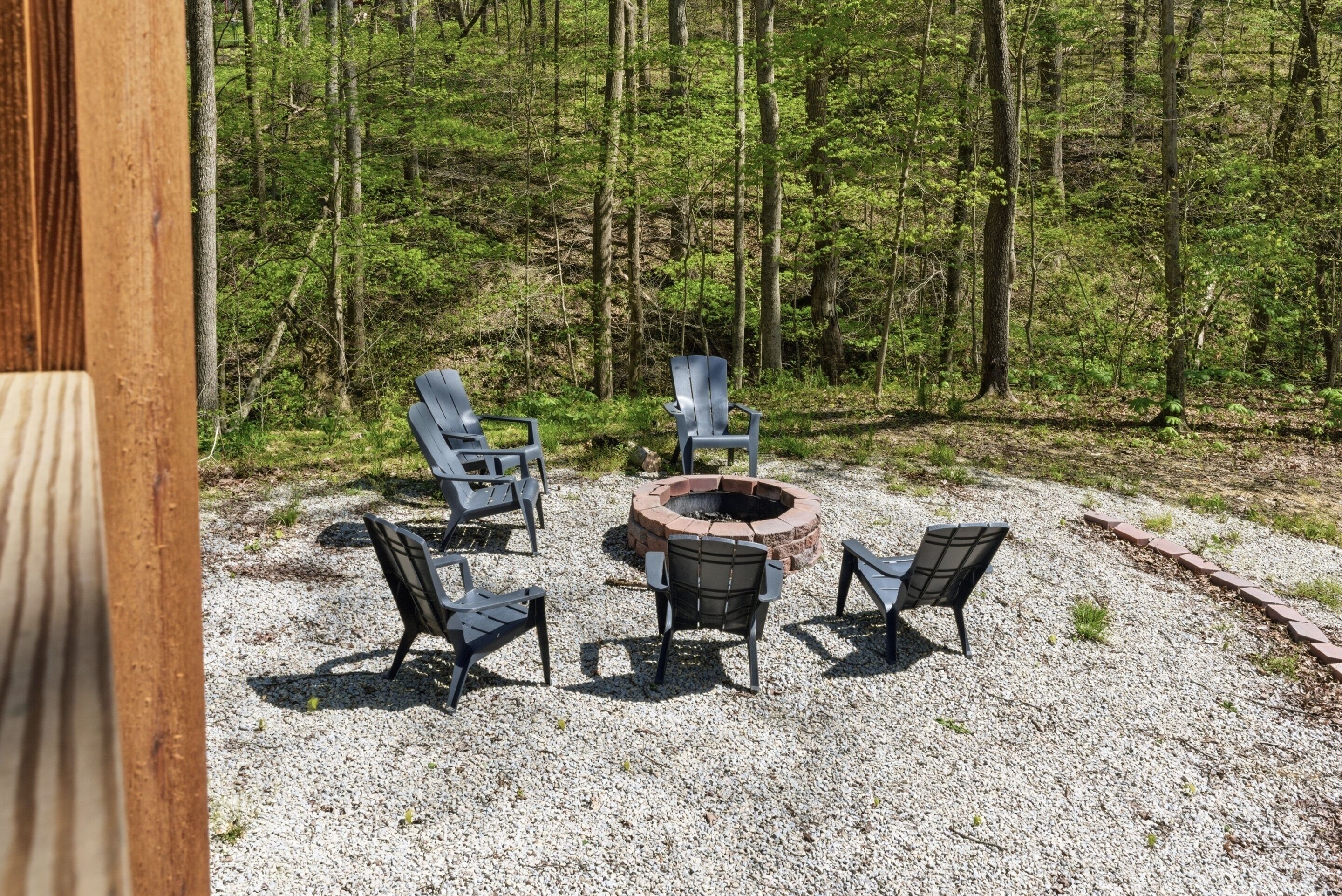 Un espace de sièges disposés en cercle autour d’un foyer, entouré de gravier, avec une forêt en arrière-plan.
