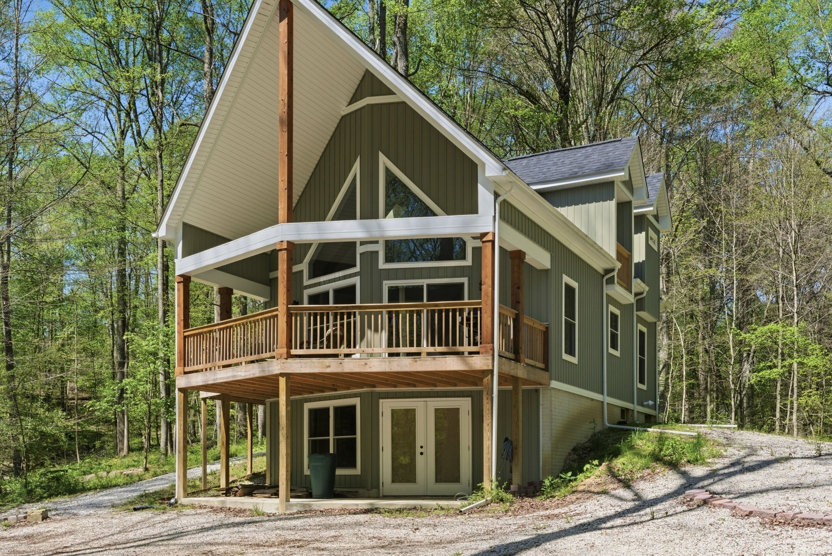 A two-story cabin with a balcony, surrounded by a forest.