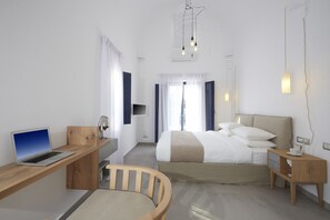 A modern hotel room with a bed, a desk with a laptop, a chair, bedside tables, and a hanging light fixture. - Amor Hideaway Villas by Mr and Mrs White (Santorini)