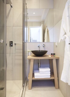 A modern bathroom with a glass-enclosed shower, a wooden vanity with a black vessel sink, and a white robe hanging on the wall. - Amor Hideaway Villas by Mr and Mrs White (Santorini)