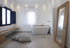 A modern bathroom with a freestanding bathtub, a bench, and a mirror. - Amor Hideaway Villas by Mr and Mrs White (Santorini)