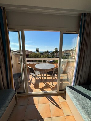 Ein Balkon mit Tisch und Stühlen, einer Couch und Blick auf Gebäude und Palmen.