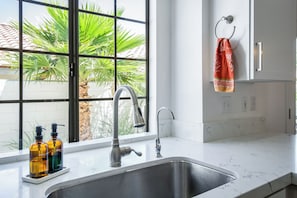 Eine Küche mit Spüle, Wasserhahn und Fenster mit Blick auf Palmen.