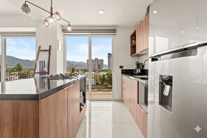 Eine moderne Küche mit einer zentralen Kochinsel, Edelstahlgeräten und großen Fenstern mit Blick auf die Stadt.