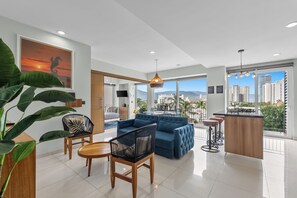 A modern living room with a sofa, chairs, a dining table, and a kitchen area with a bar. - Stylish Zoho Skies 2-BDR, Rooftop Pool + Parking (Puerto Vallarta)
