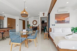 Ein modernes Hotelzimmer mit einem Bett, einer Essecke mit Stühlen und Tisch, einer Küchenzeile und einem großen Fenster mit Sonnenuntergangsblick.