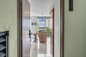 Un couloir menant à une cuisine avec vue sur de hauts immeubles et donnant sur un balcon.