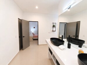 A modern bathroom with a large mirror, two black sinks, and a white countertop. - Cozy 2BR Near Malecón Rooftop Terrace (Jalisco)