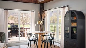 A dining area with a round table, four chairs, a vase with dried plants, and a cabinet with glass doors.