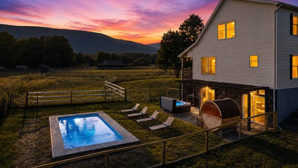 A two-story house with a swimming pool, outdoor seating, and a hot tub.