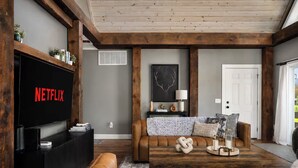 A living room with a large flat-screen TV, a brown leather sofa, a wooden coffee table, and a fireplace.