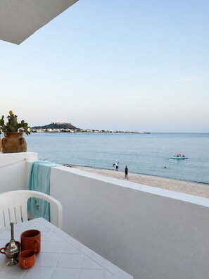A balcony with a view of the sea, a table with a teapot and cups, and a cactus plant.