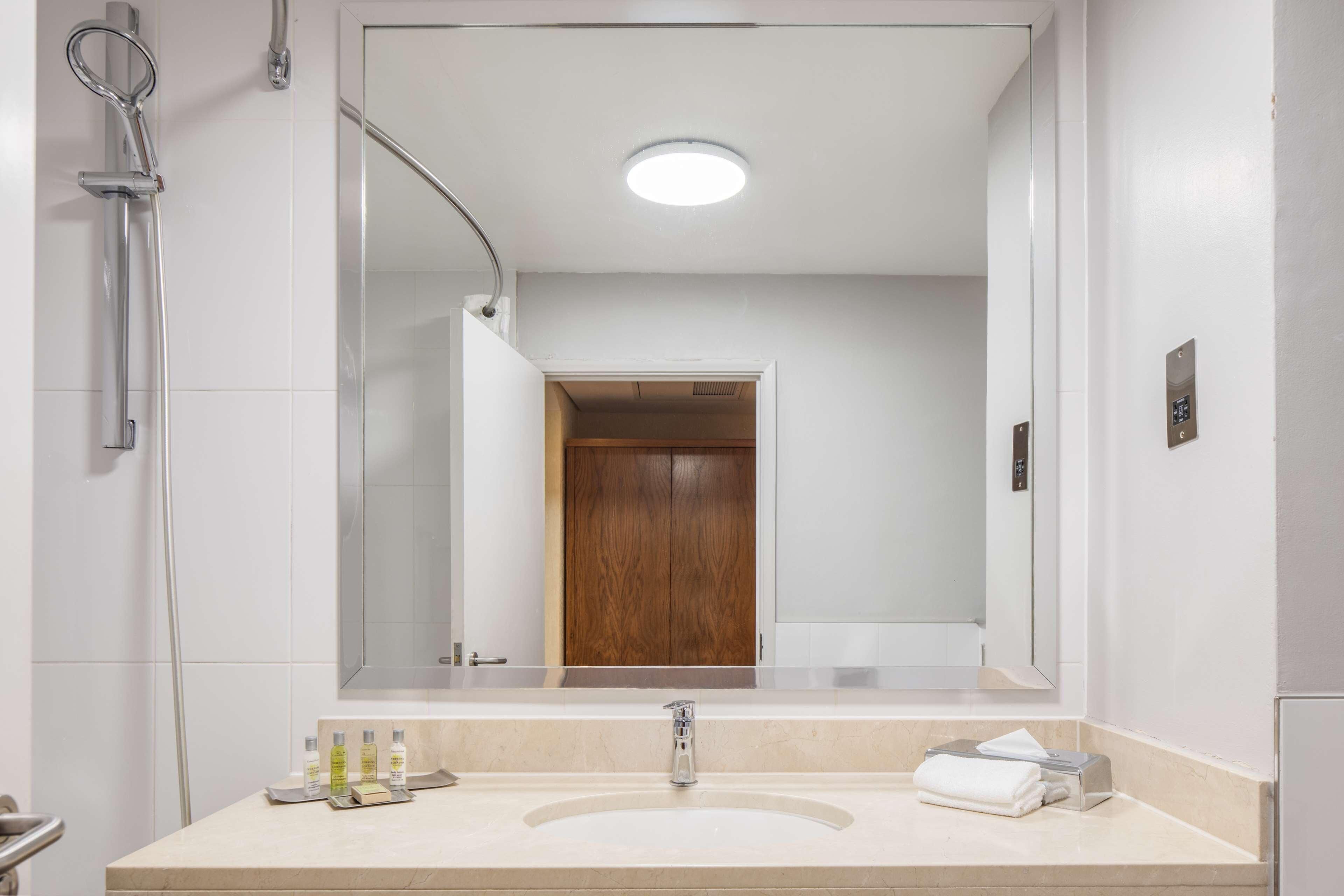 A modern bathroom with a large mirror, a shower, and a sink with toiletries.