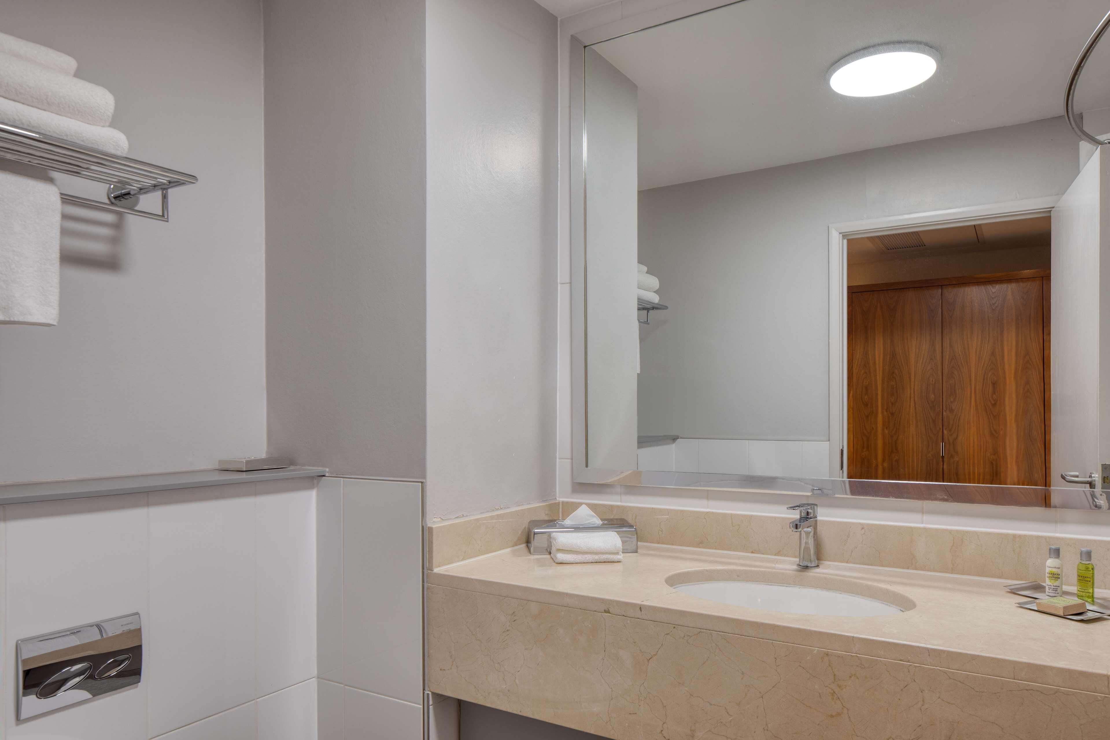 A bathroom with a double sink, a mirror, a towel rack, and a wooden door.