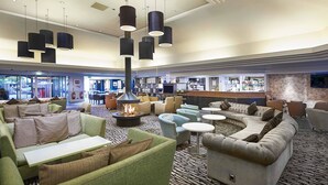A modern lounge area with sofas, armchairs, a central fire feature, and a bar area in the background. - Doubletree Newbury North (Newbury)