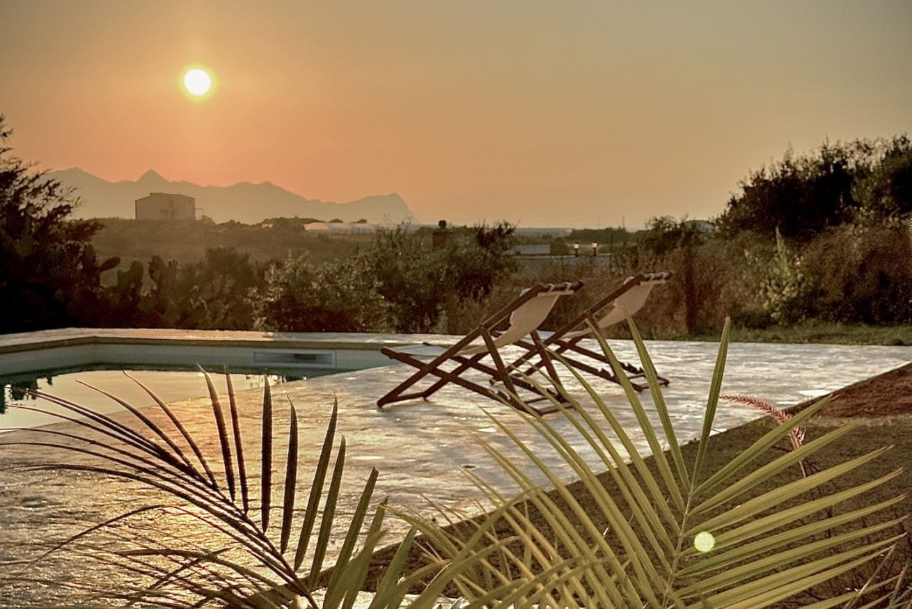 A pool with lounge chairs, a clear sky, and mountains in the background.