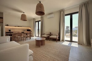 Ein modernes Wohnzimmer mit Sofa, Couchtisch und Essbereich mit Stühlen sowie Küchenzeile.