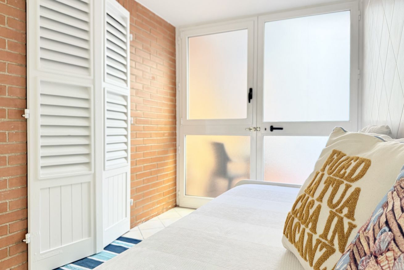 A bedroom with a brick wall, a white door with shutters, a bed with a white comforter, and a pillow with text.