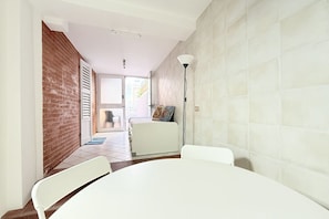 A room with a white table, two white chairs, a white sofa, a brick wall, a tiled floor, and a door leading to a balcony.