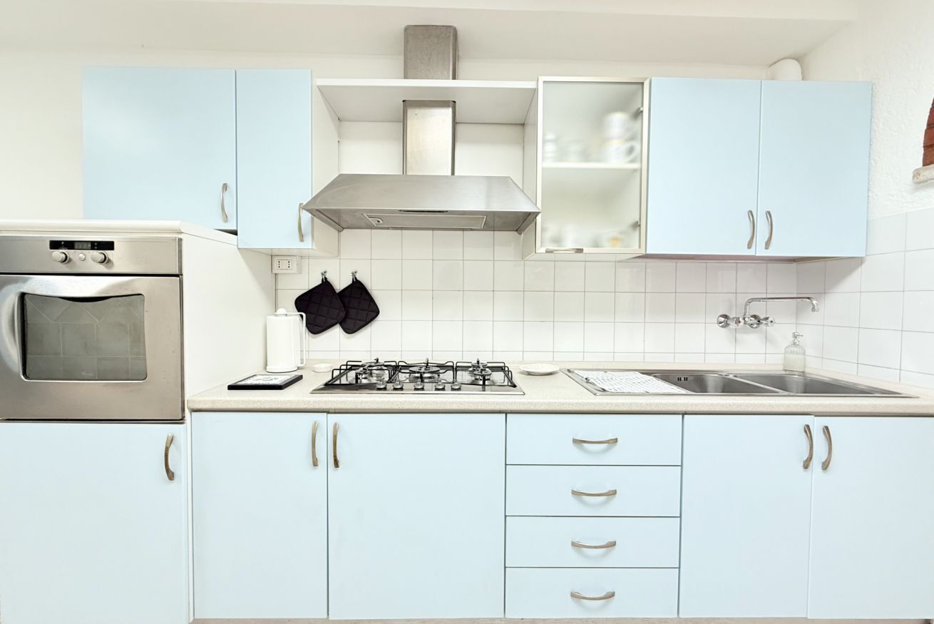 A kitchen with white cabinets, a stove, a sink, and a range hood.