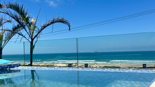 Un ciel d’un bleu éclatant, une piscine bordée de carreaux, des palmiers et, au loin, une plage.