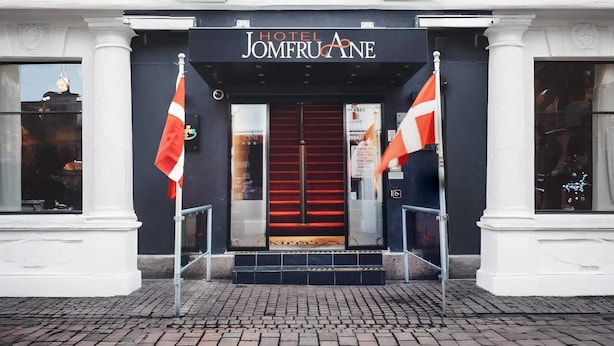 La entrada del Hotel Jomeroane, con alfombra roja, dos banderas y un toldo negro.