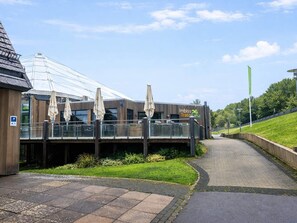 Un edificio moderno con estructura de vidrio, asientos exteriores con sombrillas y un camino que lo lleva a él.
