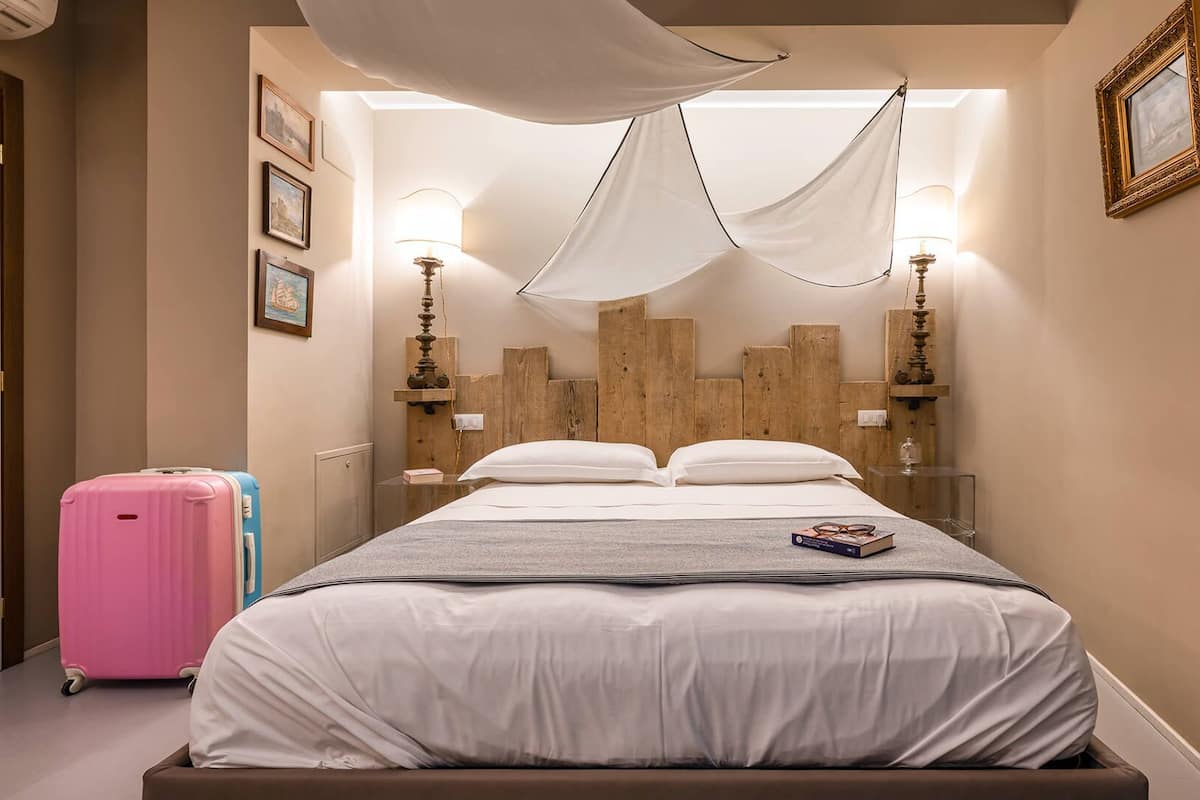 A hotel room with a bed, a wooden headboard, bedside lamps, a suitcase, and a framed picture on the wall.