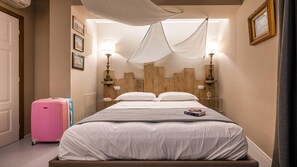 A hotel room with a bed, a wooden headboard, bedside lamps, a suitcase, and a framed picture on the wall. - A'mare Luxury Rooms (Diano Marina)