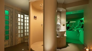 Ein Spa-Raum mit Steinwand, einer großen Säule und einem grün beleuchteten Bereich, in dem zwei Personen sitzen.
