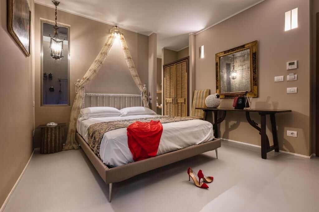 A bedroom with a canopy bed, a bedside table, a mirror, and a door.