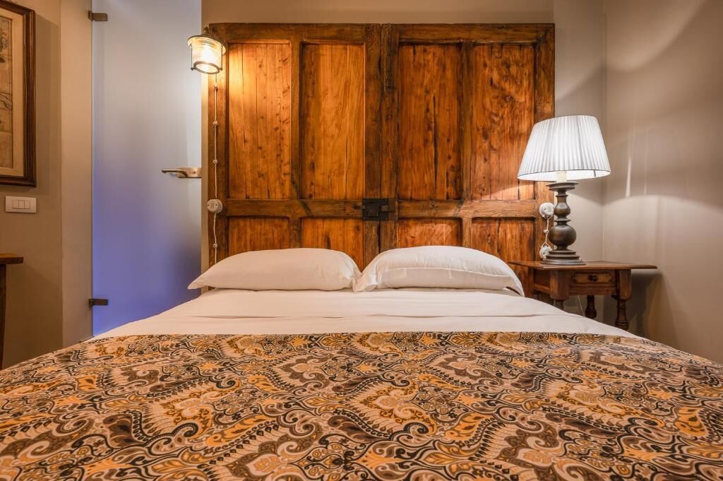 Ein Zimmer mit einem Bett, einer Holztür, einem Nachttisch mit Lampe und einer Wandleuchte.