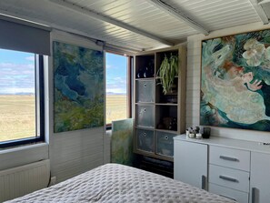 Ein Schlafzimmer mit großem Fenster, einem Bett, einer Kommode und zwei Bildern.