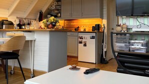 Eine Küche mit weißer Arbeitsplatte, einem Kühlschrank, einer Mikrowelle und einem Essbereich mit einem Stuhl.