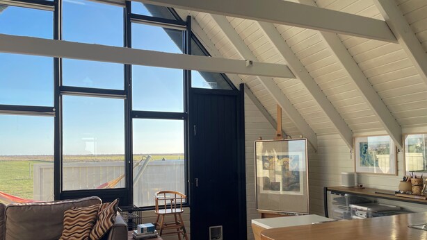 Ein geräumiges Loft mit großen Fenstern, einer gemütlichen Sitzecke, einer Küche mit Holztresen und Blick auf die Landschaft.