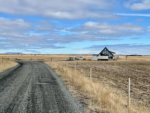 Une route de campagne mène à une maison moderne dotée d’un toit en pente et de grandes fenêtres.