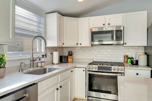 A modern kitchen with white cabinetry, a stainless steel stove, a microwave, and a sink.