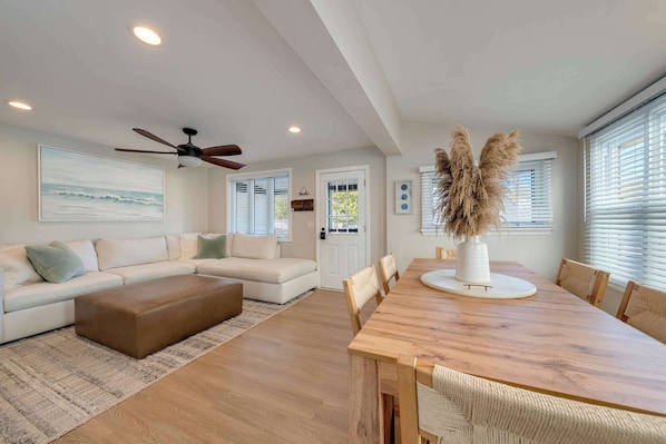 A modern living room with a sectional sofa, a wooden dining table, and a ceiling fan.