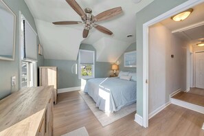 A bedroom with a ceiling fan, a bed, a desk, and a window with blinds.