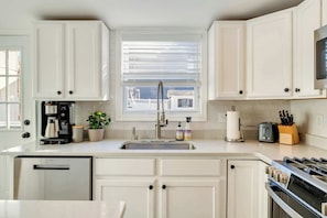 A kitchen with white cabinets, a stainless steel sink, a coffee maker, a toaster, and a stove.