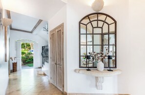 A hallway with a large arched mirror, a stone bench, and a door leading to a staircase.